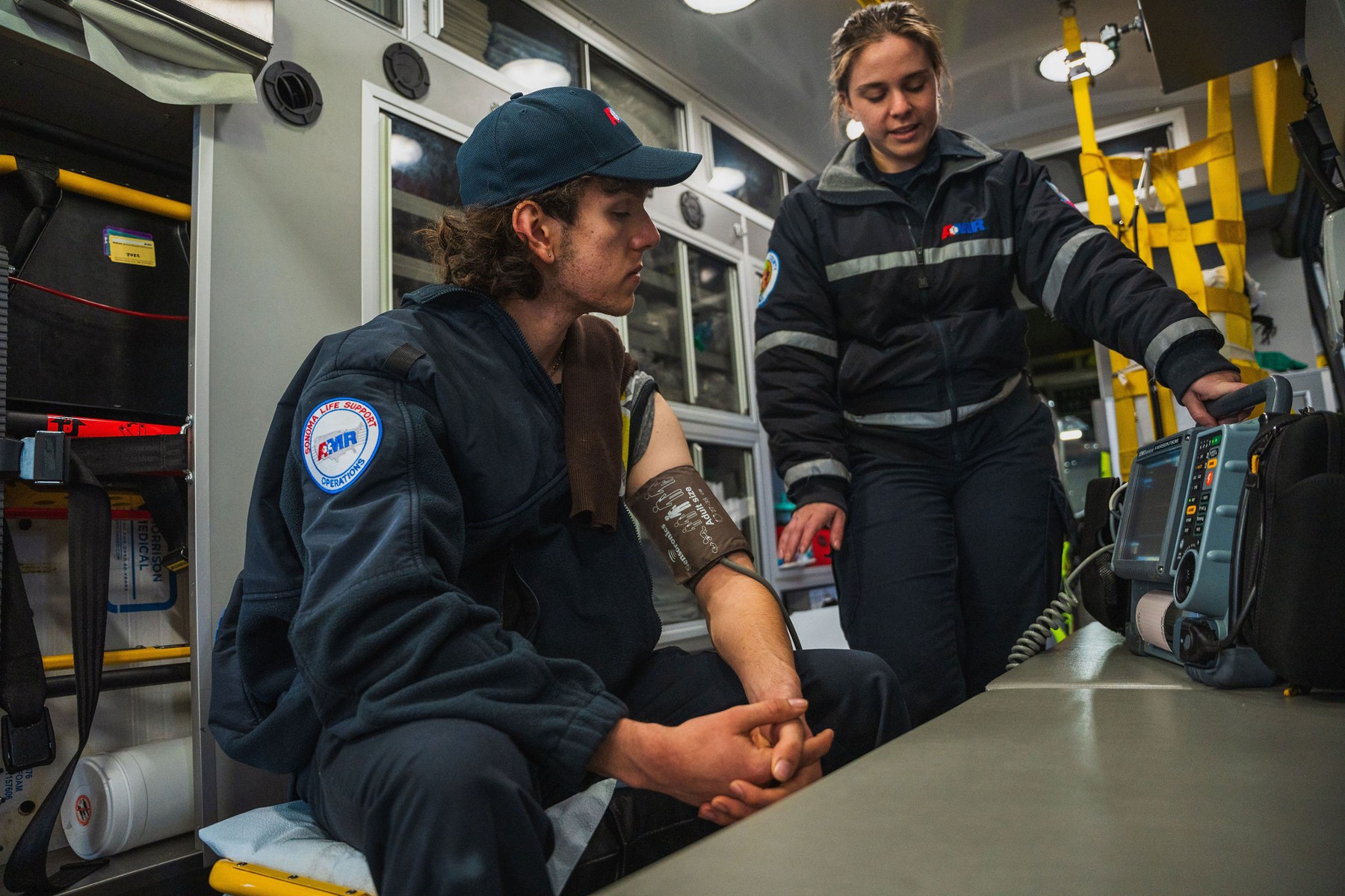 A mentor demonstrating a blood pressure monitor inside an ambulance