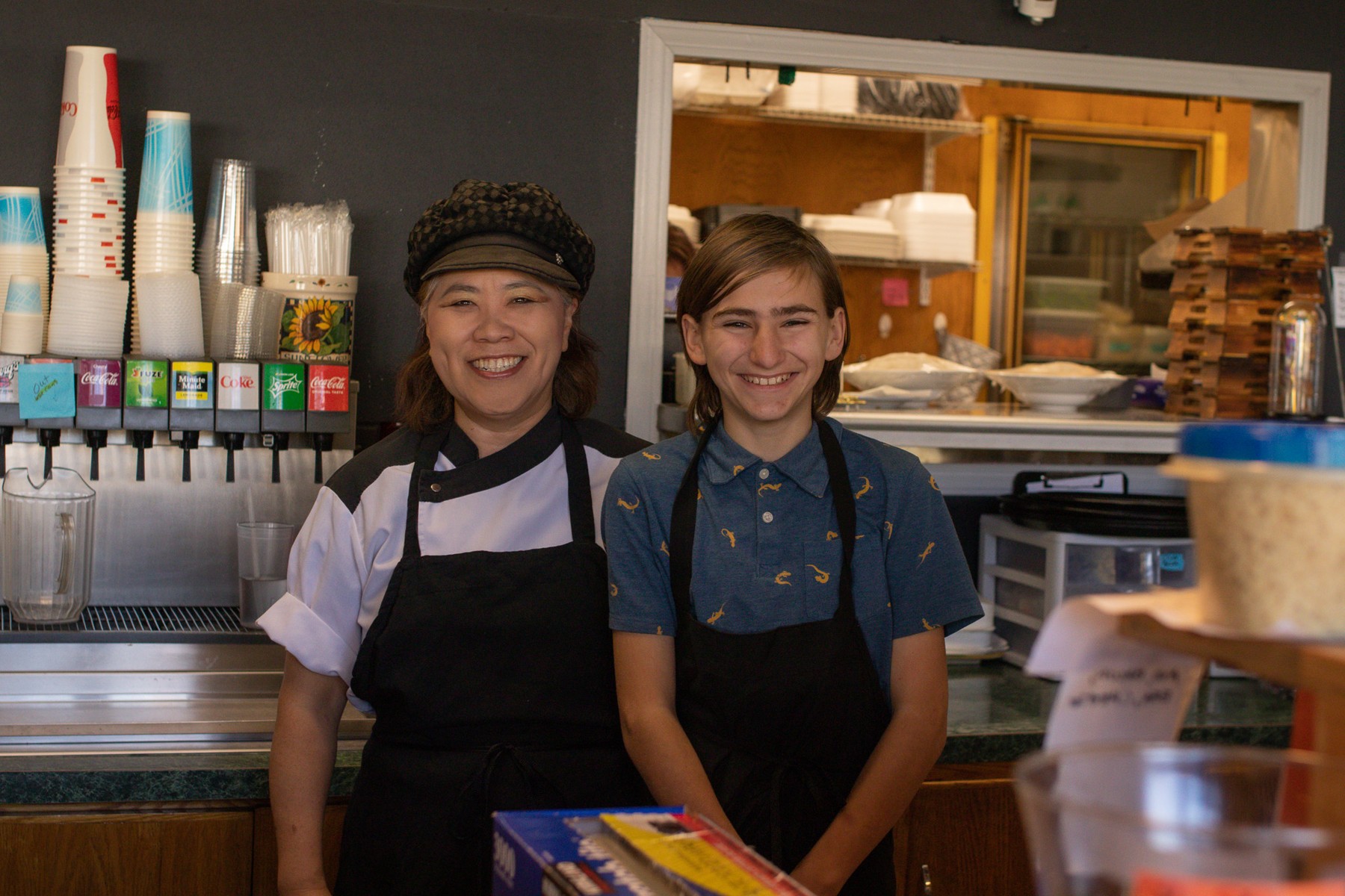 Two people wearing aprons behind a café counter